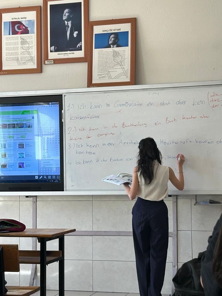 Professora de costas escrevendo na lousa com o livro na mão